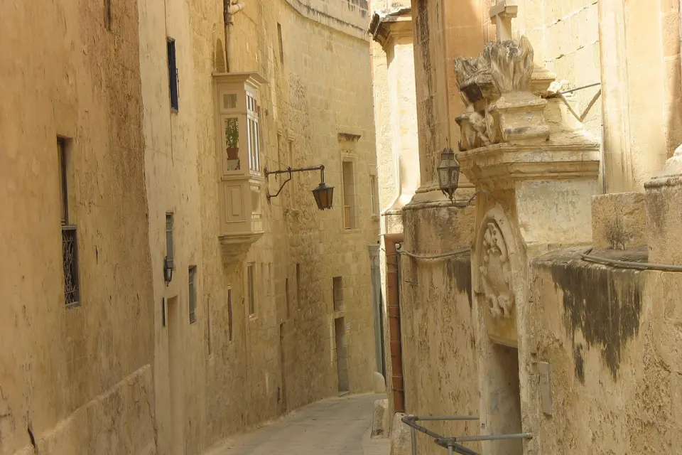 Narrow limestone alley with a wooden balcony in Mdina, Malta